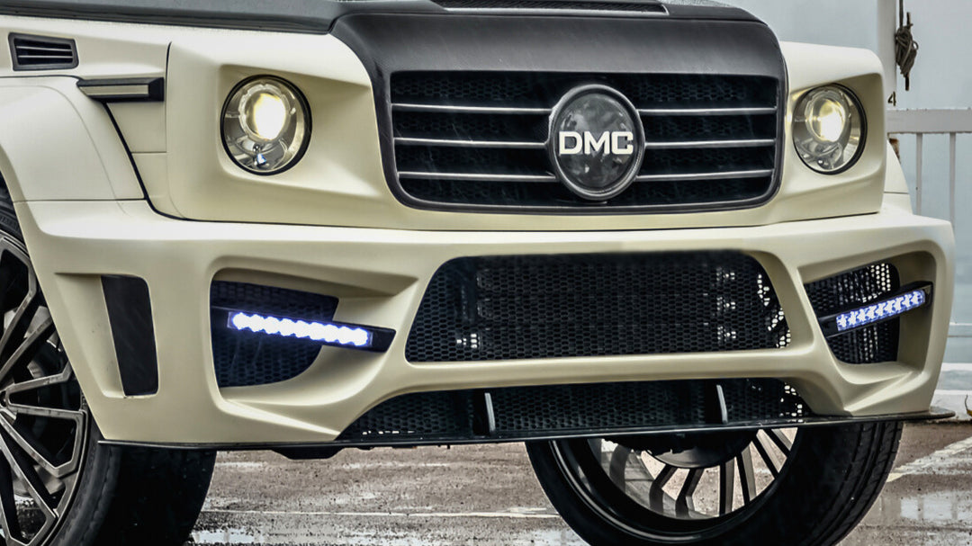 Front close up of DMC Zeus Front Bumper: Forged carbon/Kevlar options for Mercedes-AMG G63 W463 (2019-2025). Aggressive styling, integrated LEDs. installed on an off white G-wagon