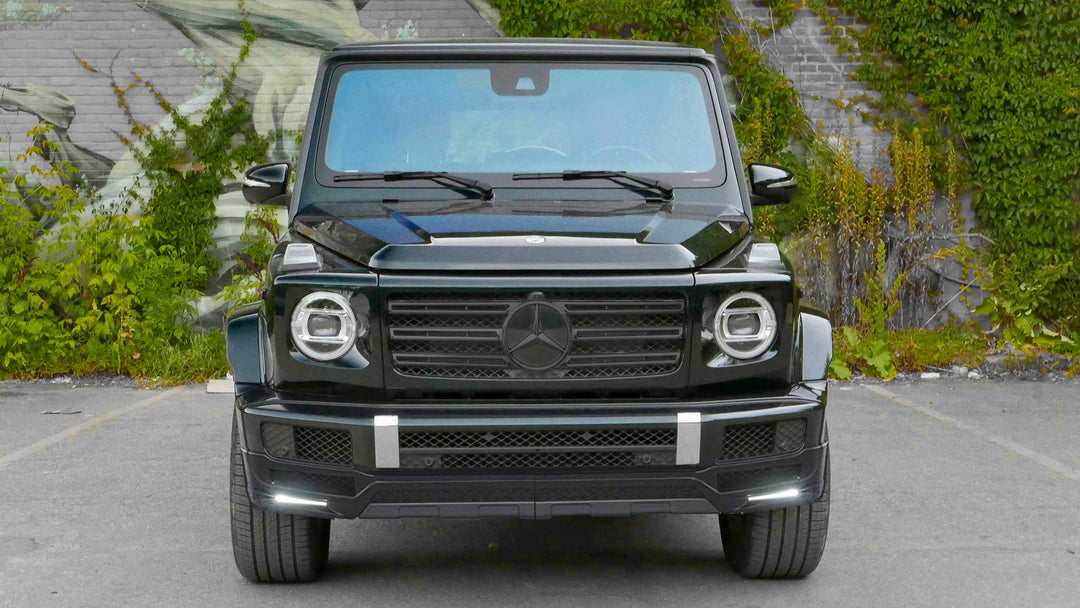 DMC 3-piece carbon fiber front lip spoiler for 2019+ Mercedes-Benz G-Class W463A/W464 (G500/G550) installed on a black g-wagon parked in front of a mountain