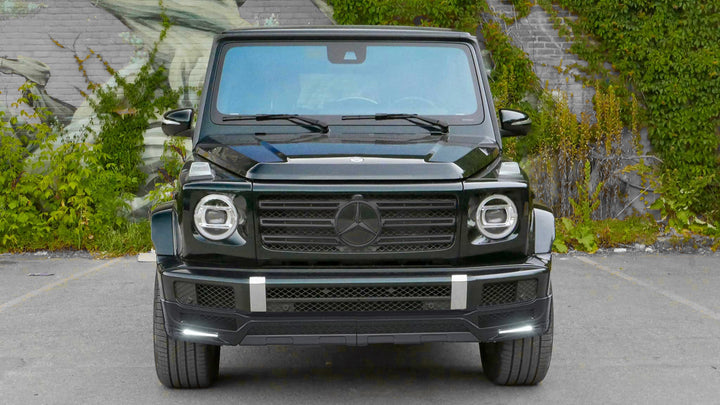 DMC 3-piece carbon fiber front lip spoiler for 2019+ Mercedes-Benz G-Class W463A/W464 (G500/G550) installed on a black g-wagon parked in front of a mountain