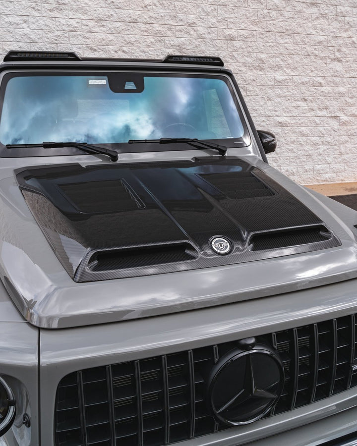 Urban Automotive carbon fiber hood mounted on Mercedes-AMG G63, enhancing performance cooling and aggressive styling.