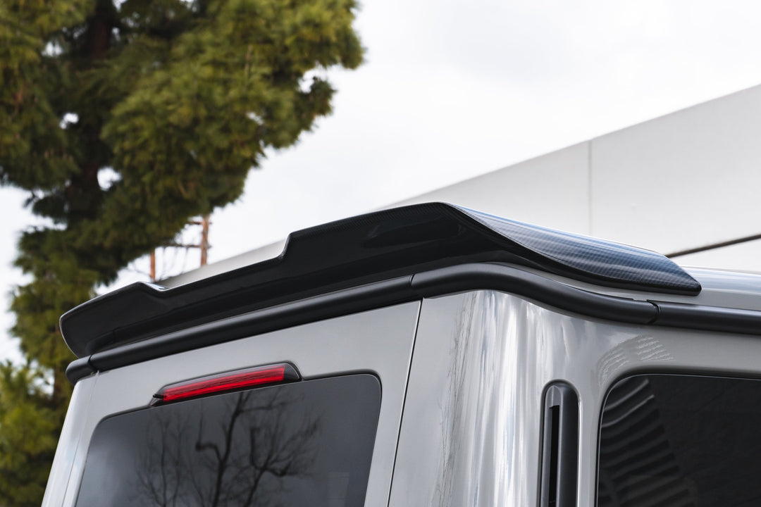 Textured carbon fiber surface of Urban Automotive rear spoiler for G-Class, showcasing aerodynamic design.