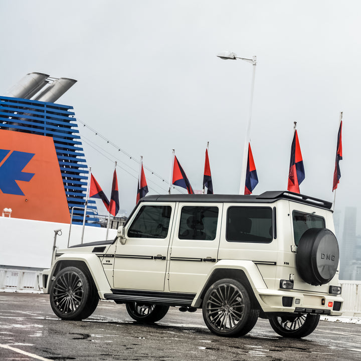 DMC ZEUS Carbon Wide Body Fenders installed on black AMG G63 W463 whole car side view parked in a lit with several flags in the background