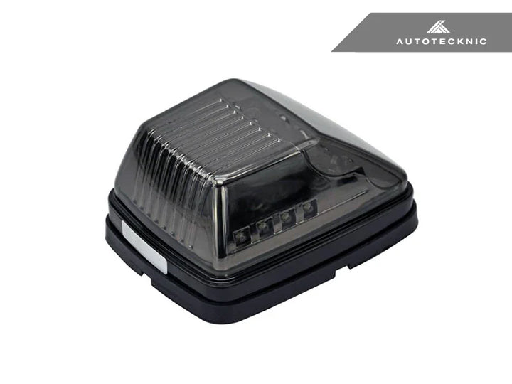 single Close-up of AutoTecknic smoked lens housing for G-Class turn signals - modern blackout finish complements carbon fiber mirror caps on a white background with autotecknic logo on the top right