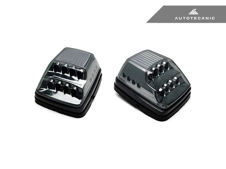 pair of Smoked LED turn signal lights installed on Mercedes-Benz G-Class W463 front bumper - plug-and-play replacement with amber SMD LEDs and 180° visibility on a white background with autotecknic logo on the top right 