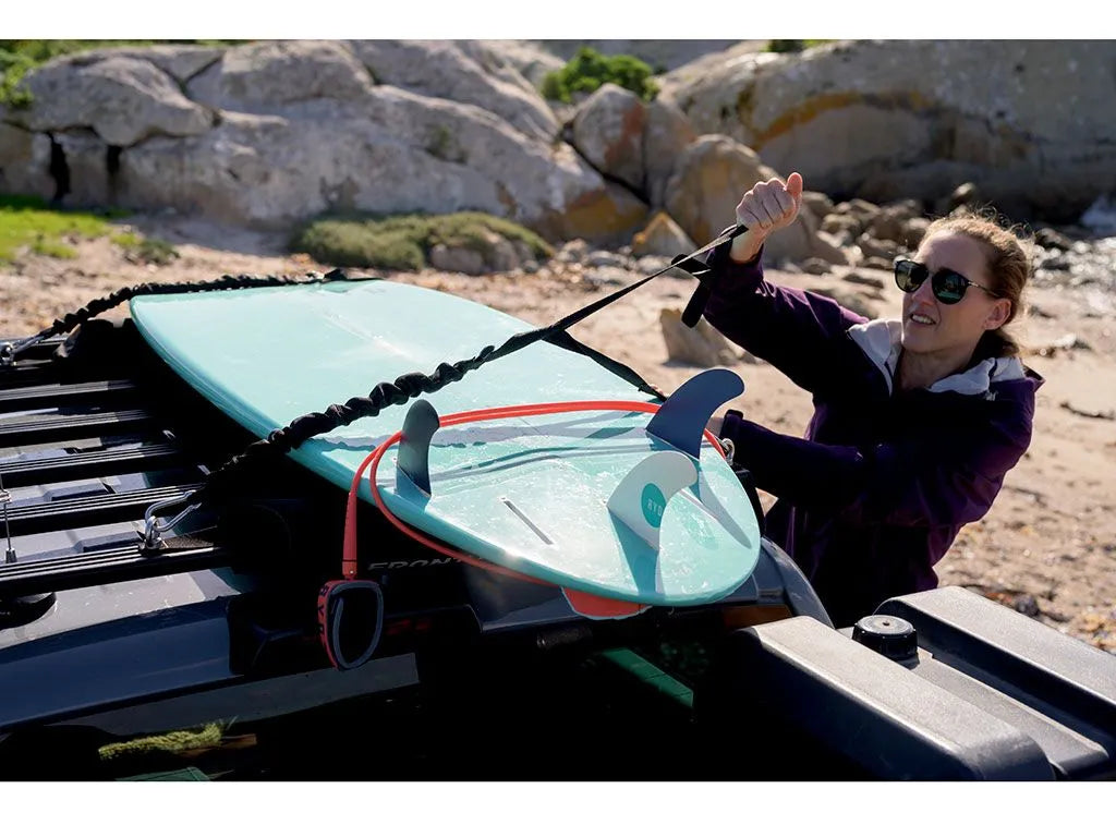 Stratchits in use, fastening a surfboard and camping chairs to a roof rack without over-tightening or damaging equipment